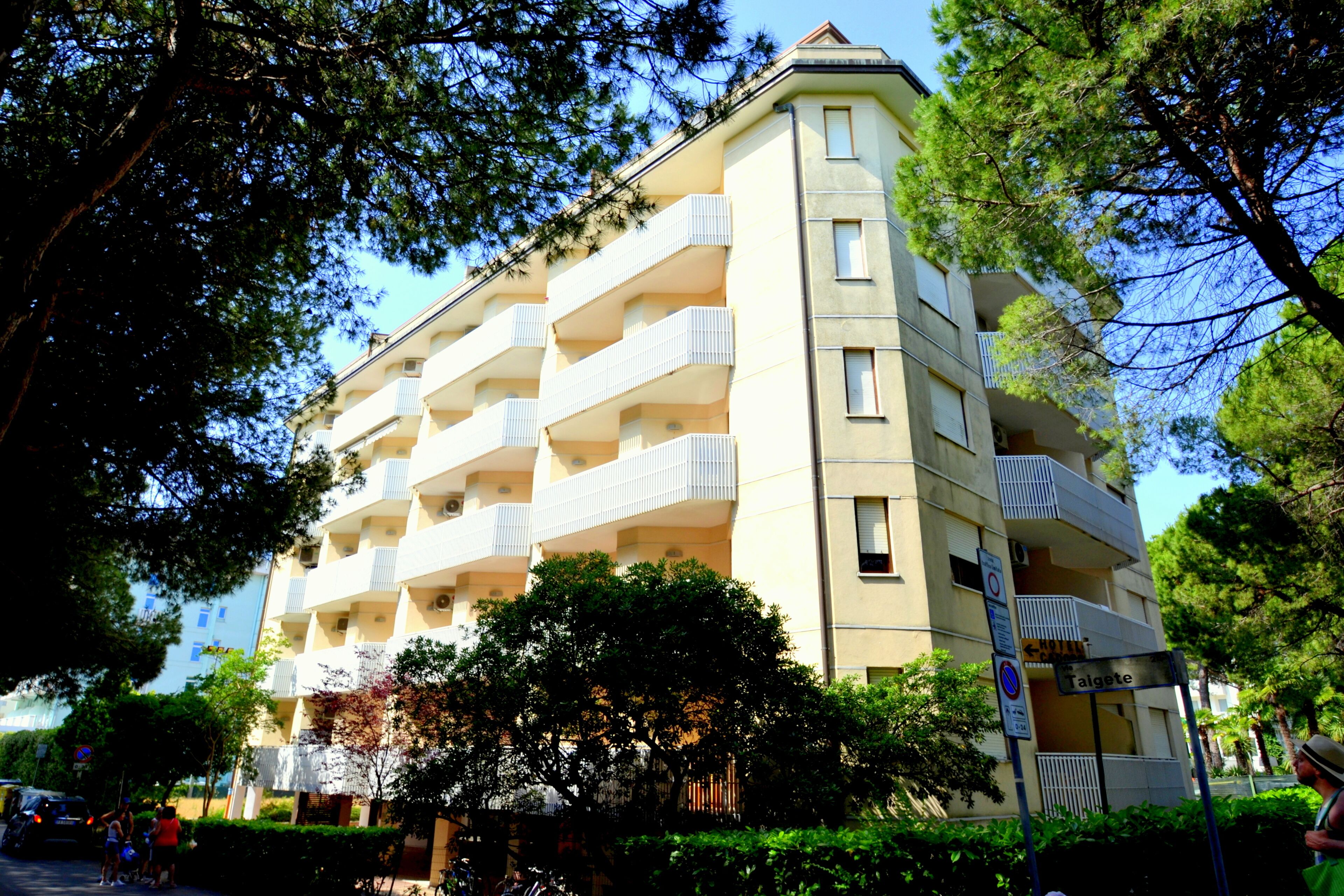 A multi-story building with balconies, surrounded by trees and greenery.