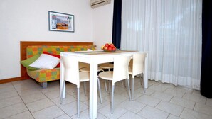 A small room with a bed, a table with chairs, a bowl of fruit, and a picture on the wall. - Coastal Comfort Flat Just 400m From the Beach (San Michele al Tagliamento)