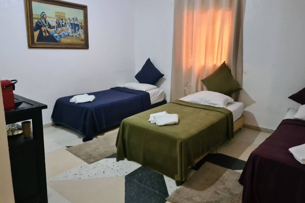 Hotellihuone, jossa on kaksi erillistä sänkyä, työpöytä, tuoli, seinällä taulu ja ikkuna, jossa on verhot.