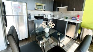 Una cucina moderna con frigorifero in acciaio inossidabile, forno a microonde, fornello e lavastoviglie. C'è un tavolo in vetro con sedie e un vaso di fiori.