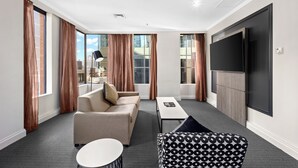 Una habitación de hotel moderna con sofá, sillón y televisión de pantalla plana.