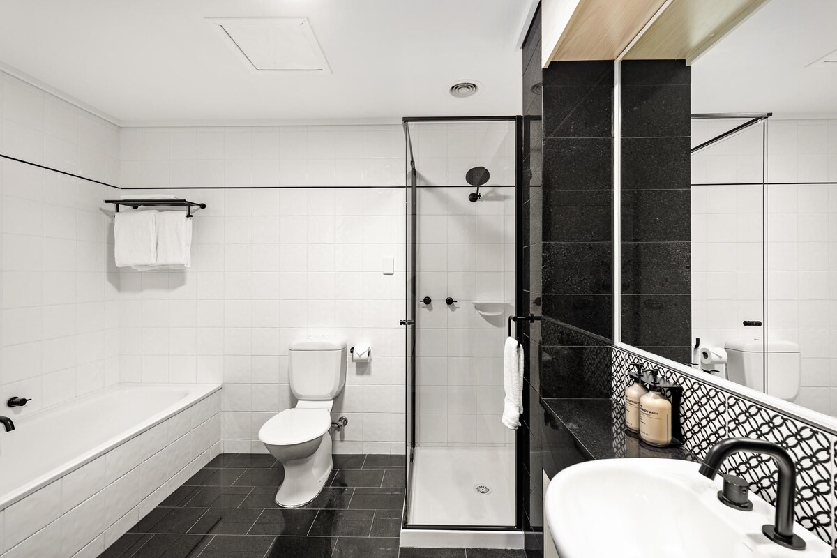 A modern bathroom with a bathtub, toilet, and glass-enclosed shower.