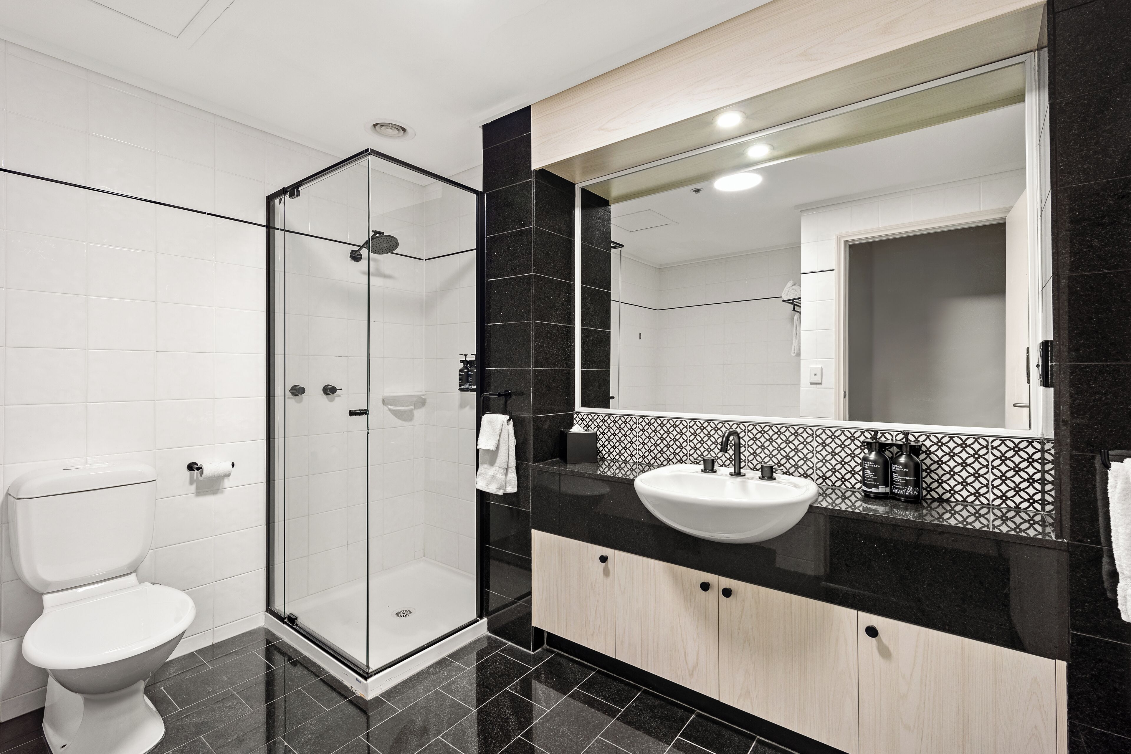Une salle de bain moderne avec une douche à parois de verre, des toilettes blanches et un lavabo sur un plan de travail noir.