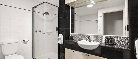 Une salle de bain moderne avec une douche à parois de verre, des toilettes blanches et un lavabo sur un plan de travail noir.
