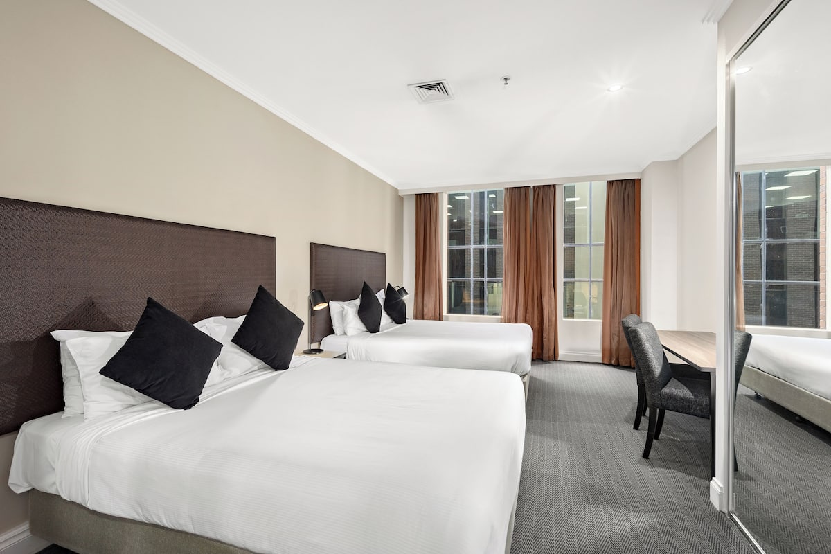Ein Hotelzimmer mit zwei Betten, einem Schreibtisch und einem großen Fenster mit Vorhängen.