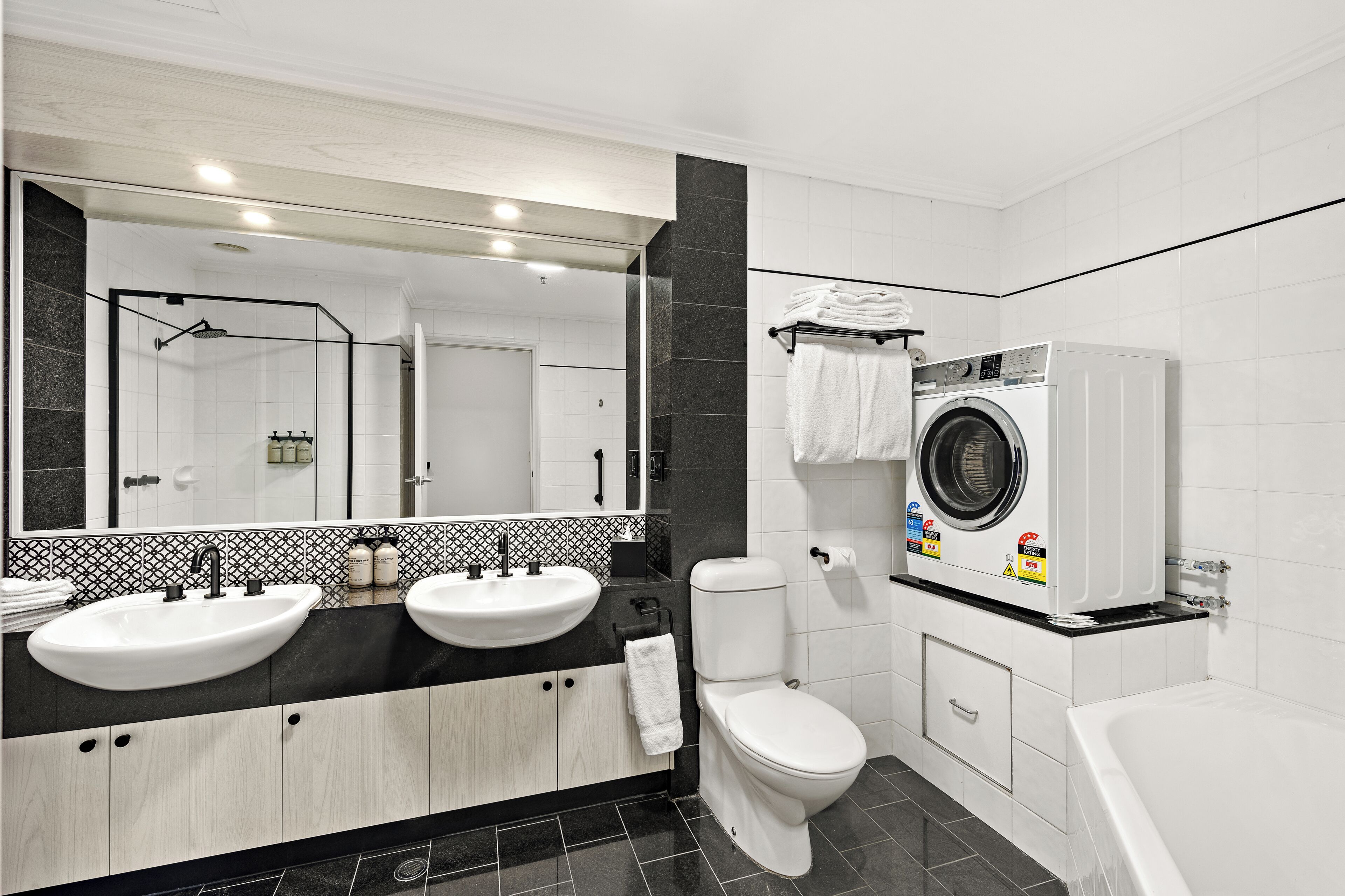 Une salle de bain moderne avec deux lavabos, des toilettes, un lave-linge et une baignoire.
