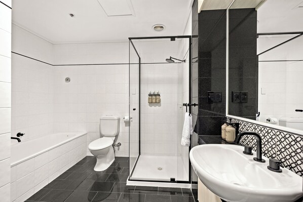 Un baño moderno con ducha envuelta en vidrio, inodoro blanco, bañera y lavamanos con grifo negro.