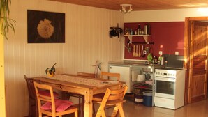 Une cuisine de taille modeste, avec une table et des chaises en bois, un poêle blanc et un mur rouge.