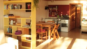 Une cuisine chaleureuse avec des meubles en bois, une table à manger entourée de chaises et une bibliothèque remplie de livres.
