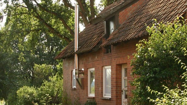Une maison traditionnelle en briques, dotée d’un toit à pente, entourée d’une végétation luxuriante et agrémentée d’une charrette en bois.
