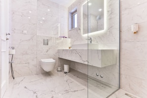 A modern bathroom with a glass shower enclosure, a toilet, and a vanity with a mirror. - Hotel Crown (Budva)