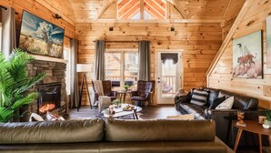 Ein gemütliches Blockhaus-Interieur mit Kamin aus Stein, Ledermöbeln und Bildern an den Wänden.