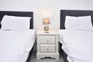 Two single beds with white linens and dark headboards, accompanied by a nightstand and lamp.