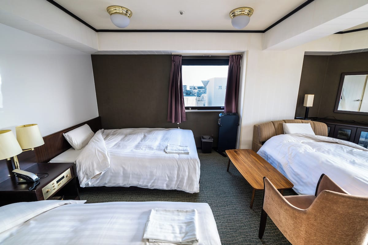 Ein Hotelzimmer mit zwei Betten, einem Schreibtisch, einem Stuhl, einer Lampe und einem fenster mit Vorhängen.