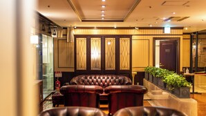 Un vestíbulo de hotel con sillones de cuero, un mostrador de recepción y un extintor.