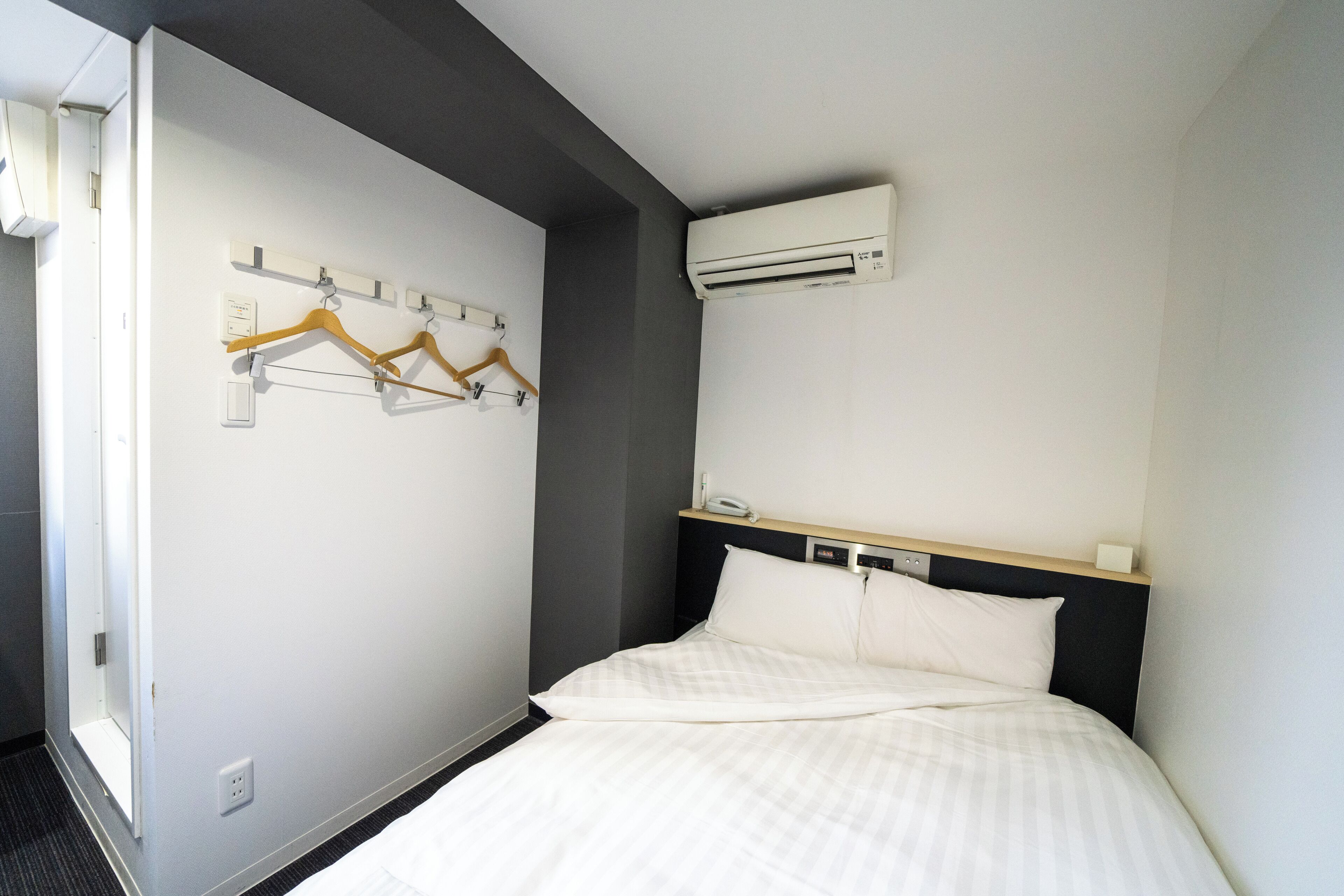 Una habitación de hotel con una cama, un aire acondicionado de pared y un perchero con perchas.