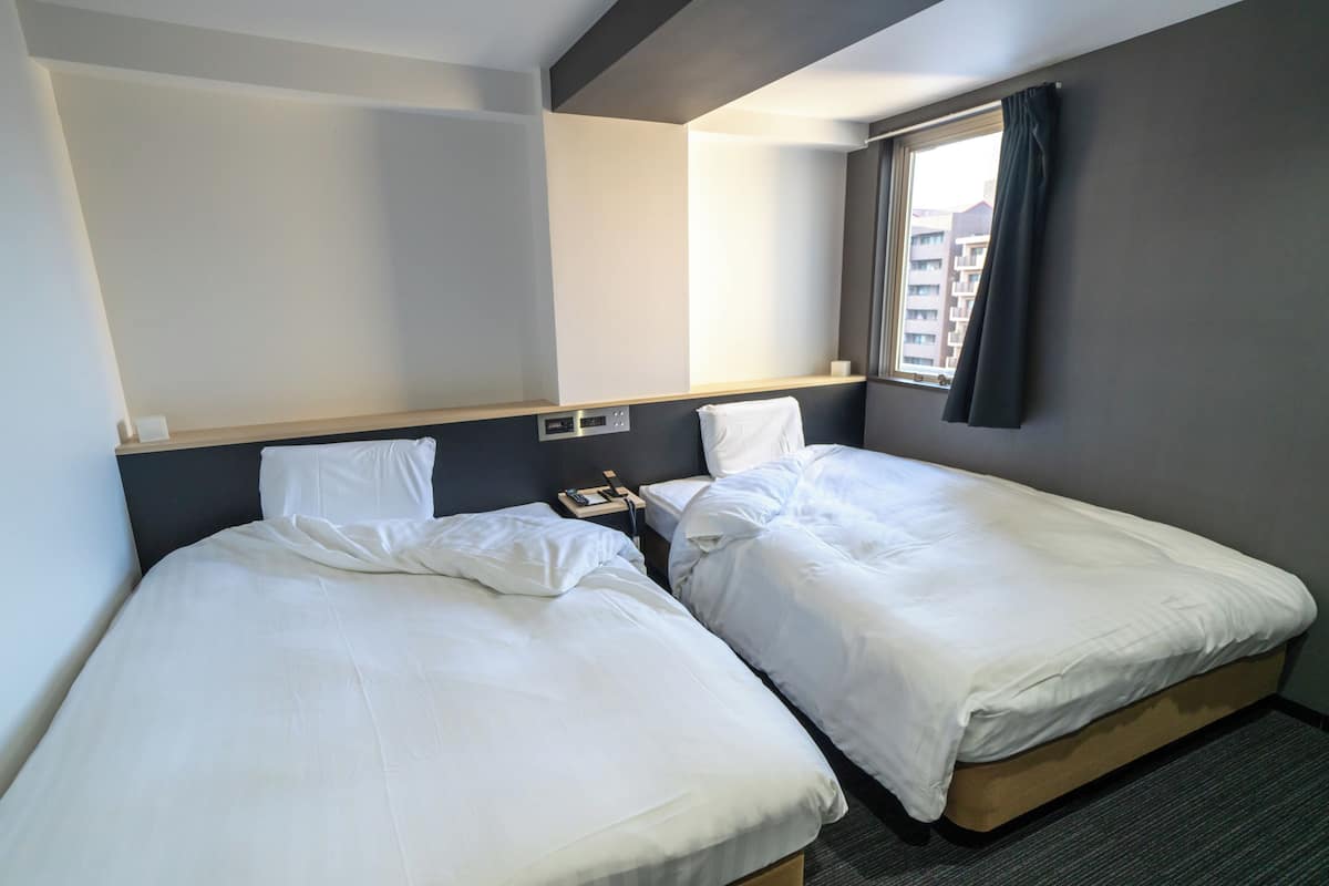 Ein Hotelzimmer mit zwei Einzelbetten, einem Nachttisch mit Telefon und einem Fenster mit Vorhängen.