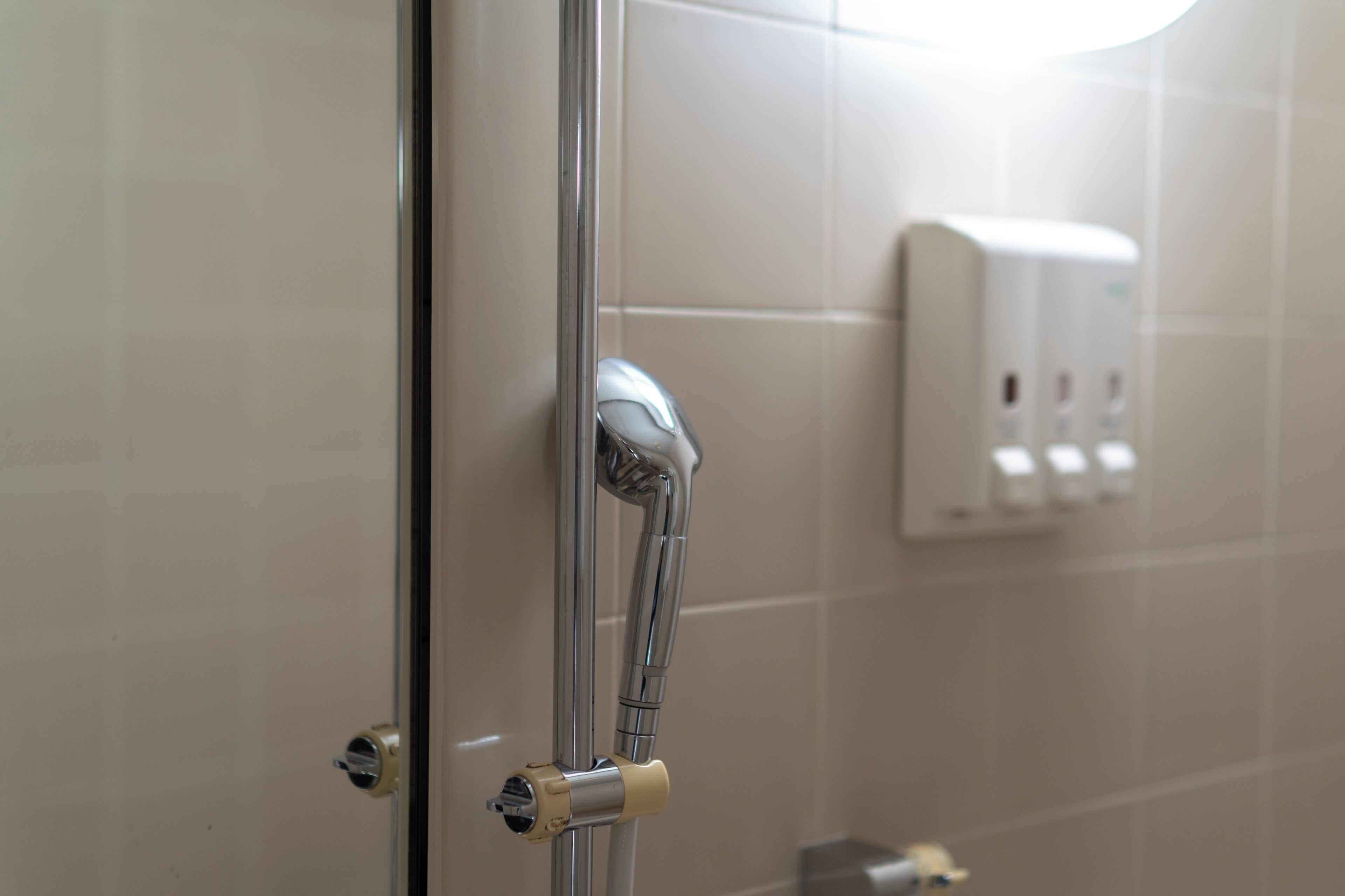 A shower with a chrome faucet and a soap dispenser on the wall.