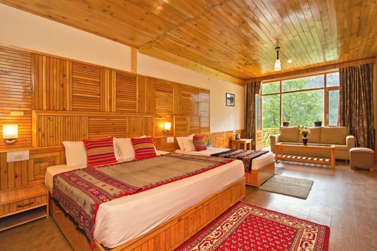 A wooden-paneled room with a large bed, two bedside tables, a sofa, and a window with curtains.