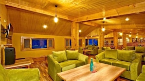 Un interior acogedor de madera con sofás y mesas verdes, ventanas amplias y una zona de bar.