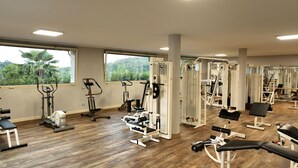 A gym with various exercise equipment, large windows, and a view of greenery. - Gardahill (Soiano del Lago)