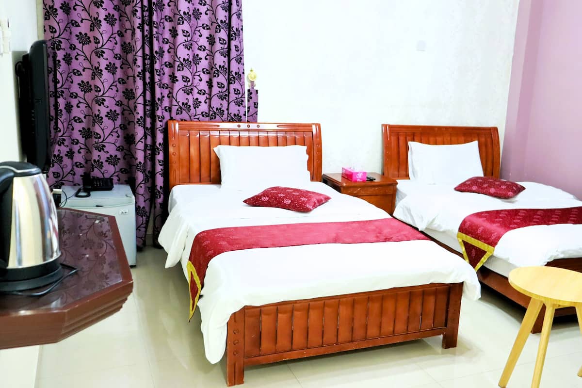 A hotel room with two wooden beds, a small wooden table, a blue chair, and a kettle on a side table.