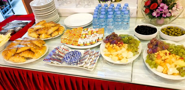 A buffet table with various food items, including pastries, fruits, and bottled water.