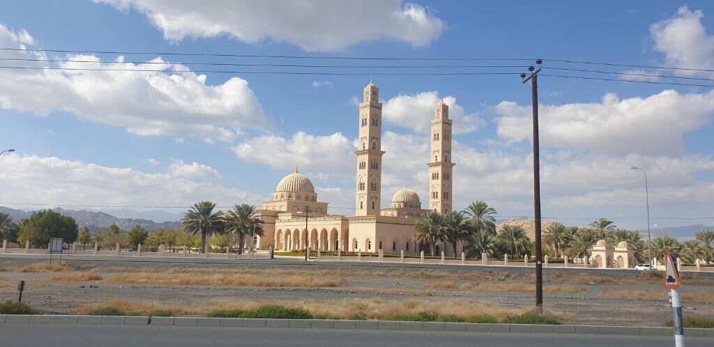 A mosque with two tall minarets and a large dome, surrounded by palm trees and a clear sky.