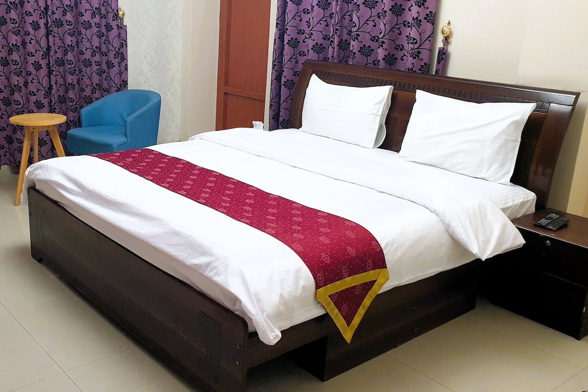 A hotel room with a bed, a blue chair, and purple curtains.