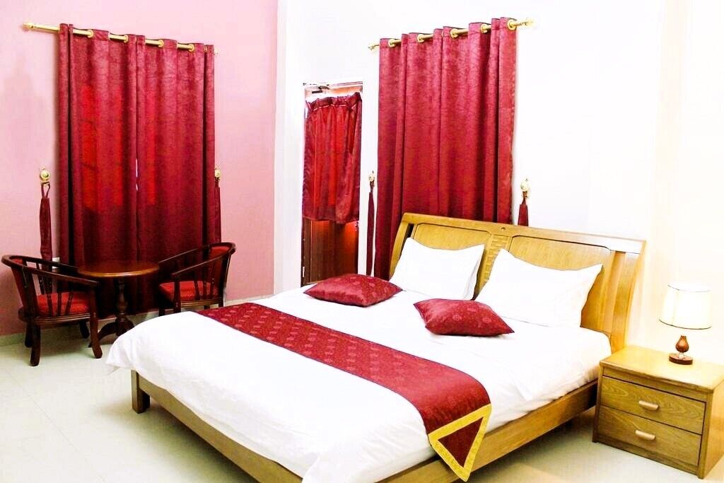 Un dormitorio con cama de madera, cortinas rojas, una mesita y un buró.