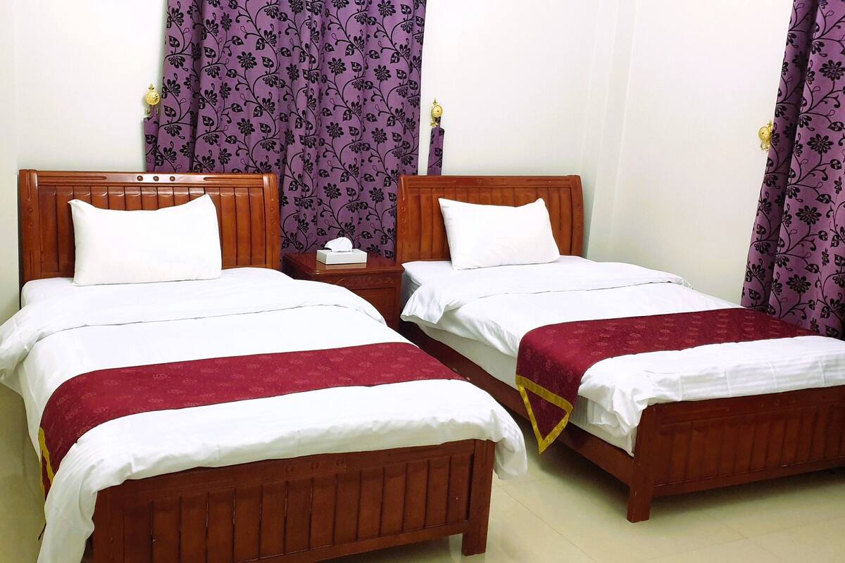 A double room with two wooden beds, each with white linens and red bedspreads.