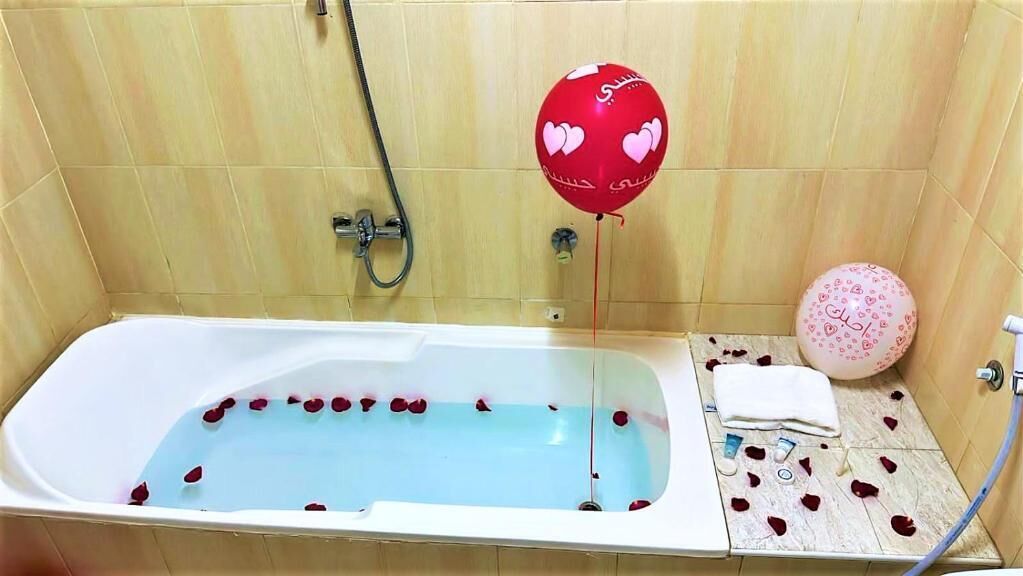 A bathtub with rose petals, a red heart-shaped balloon, and a pink ball with heart patterns.