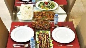 A dining table set with various dishes, including grilled meat, rice, and salads, with water bottles and cutlery. - Bahla Hotel Apartment  (Bahla)