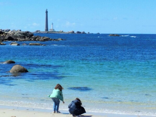 Une plage à l’eau d’un bleu cristallin, un phare et des affleurements rocheux.