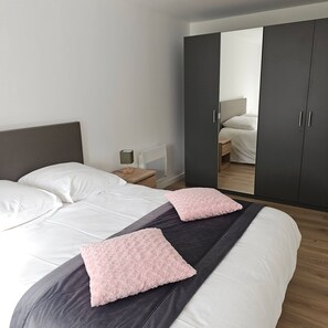 Une chambre moderne avec un grand lit, deux tables de chevet, une armoire et un miroir.