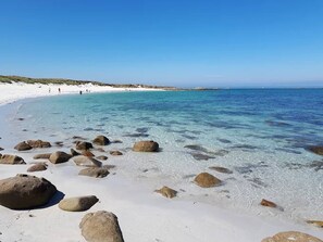 A beach with clear turquoise water, white sand, and scattered rocks.