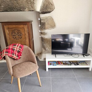 Un salon avec une télévision, un fauteuil recouvert d’une couverture à carreaux, un mur en pierre et une porte en bois ornée d’un panneau décoratif.