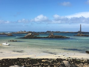 A coastal scene with a lighthouse, rocky outcrops, and a boat on the beach.