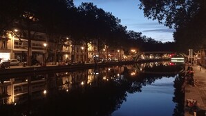 Une vue nocturne d’un canal, avec des bâtiments d’un côté et une promenade piétonne de l’autre.
