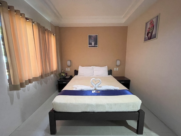 Una habitación de hotel con cama, mesita de noche, teléfono en la pared y un cuadro.