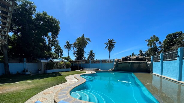 A swimming pool with a tiled edge, surrounded by a grassy area and palm trees. - Argao Seabreeze Hotel powered by Cocotel (Argao)