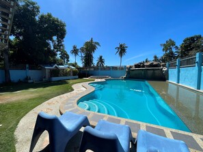 Una piscina con borde de azulejos, rodeada de césped y palmeras.
