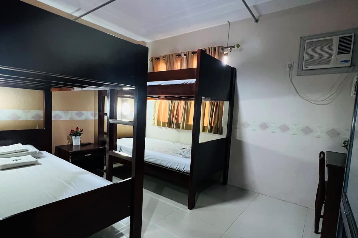 A hotel room with two bunk beds, a small bedside table, a chair, and a wall-mounted air conditioning unit.