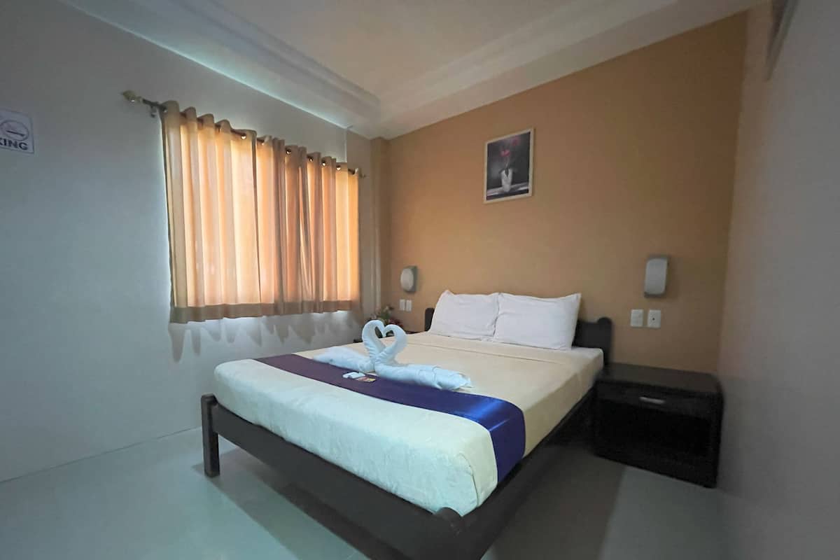 A hotel room with a bed, curtains, a wall-mounted picture, and a bedside table.