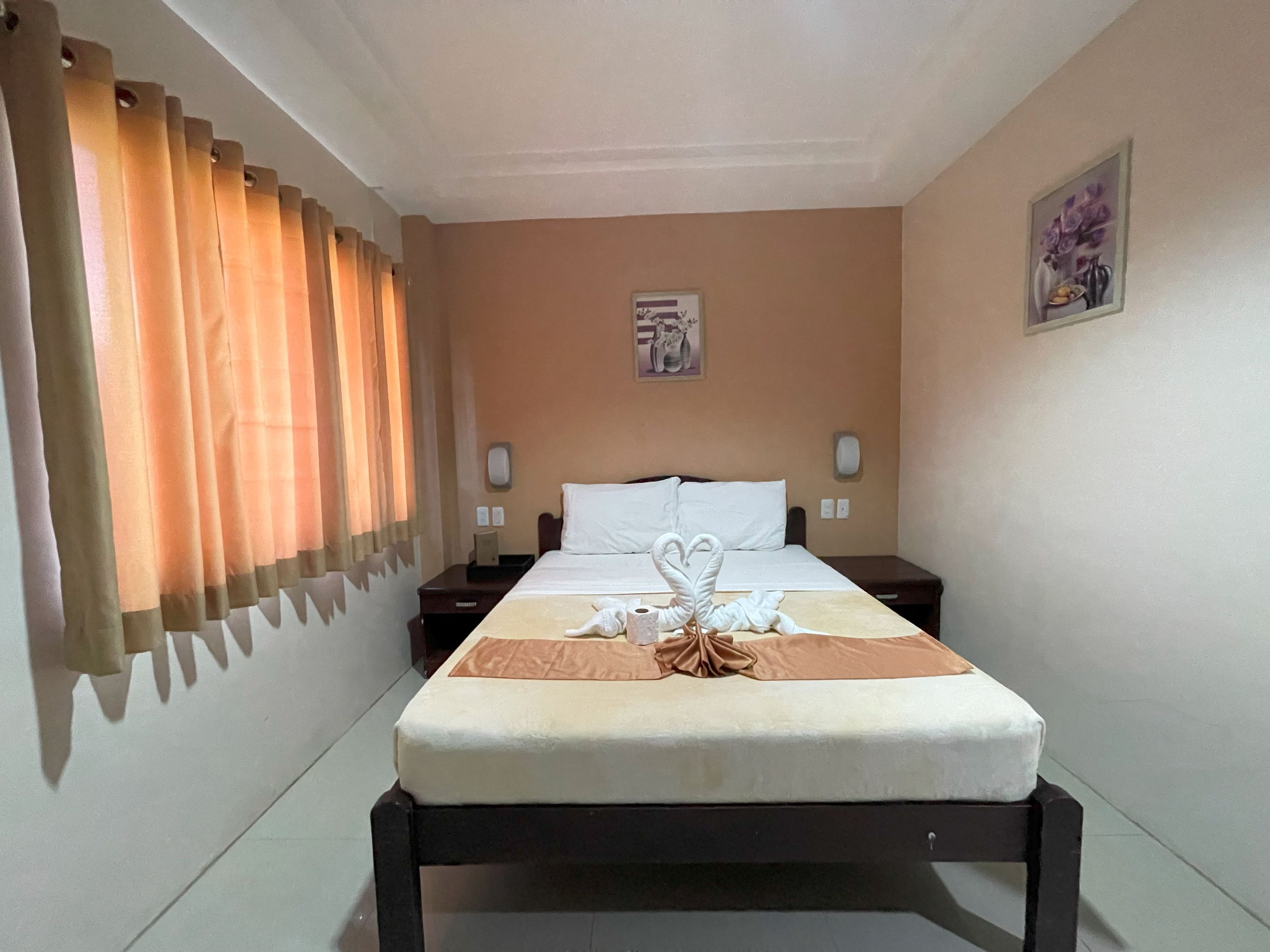 Una habitación de hotel con cama, mesita de noche, teléfono, lámpara de pared y un cuadro.