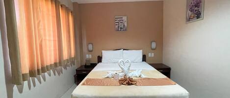 Una habitación de hotel con cama, mesita de noche, teléfono, lámpara de pared y un cuadro.