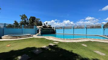 Una piscina con una cerca azul, una cascada de piedra y una zona verde con piedras para pisar.