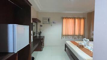 Una habitación de hotel con cama, escritorio, refrigerador, espejo y ventana con cortinas.