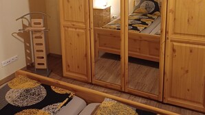 Ein hölzerner Kleiderschrank mit Spiegel, ein Bett mit gemusterten Textilien und ein kleiner Nachttisch.