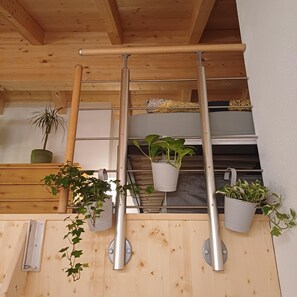 Un intérieur en bois avec une étagère en métal où sont disposées des plantes en pot et un meuble blanc.